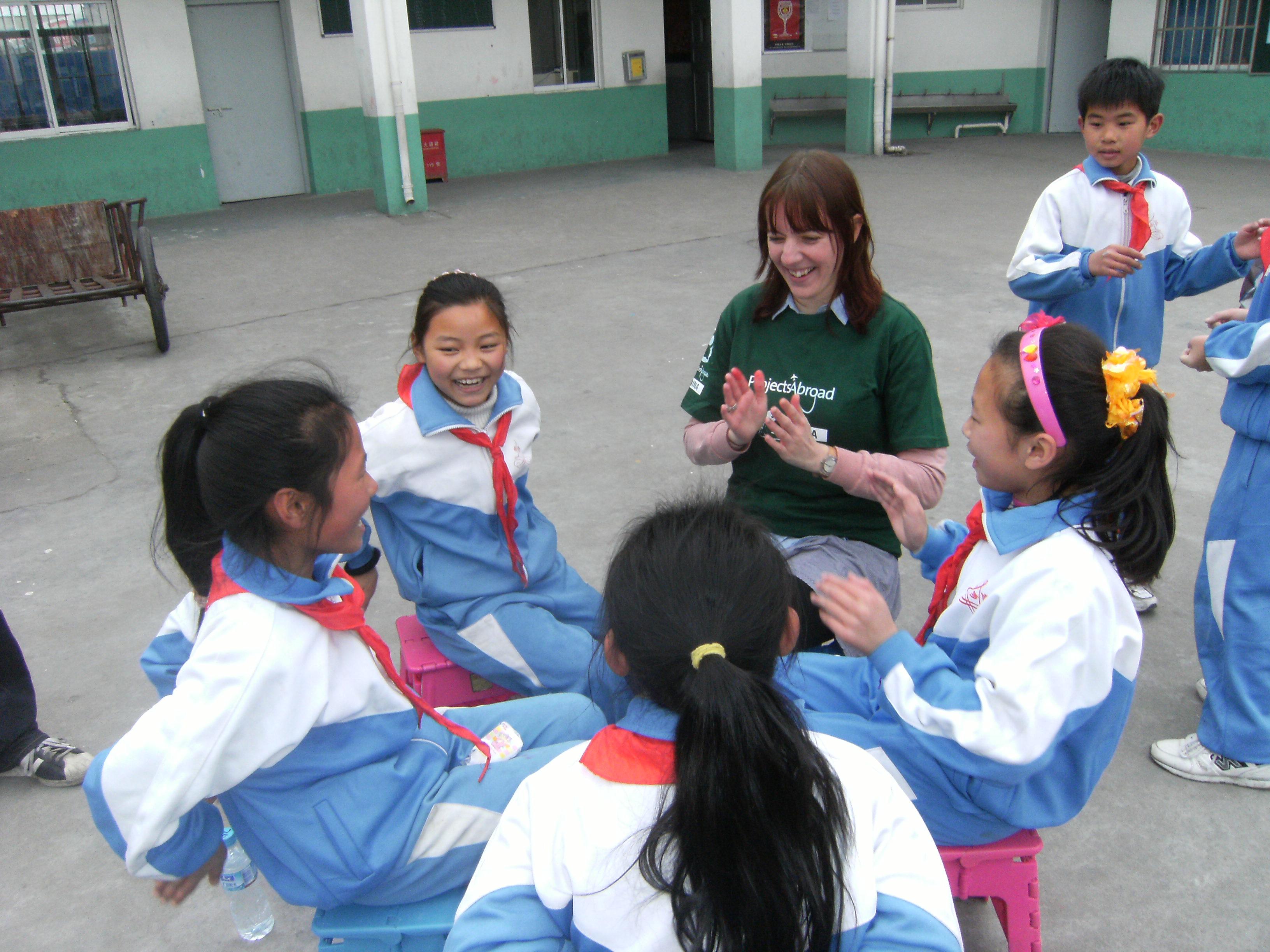 Female volunteer celebrates National Volunteer Week with children during her Childcare Project in China. Projects Abroad volunteer with children in China claps with children outside her kindergarten placement.
